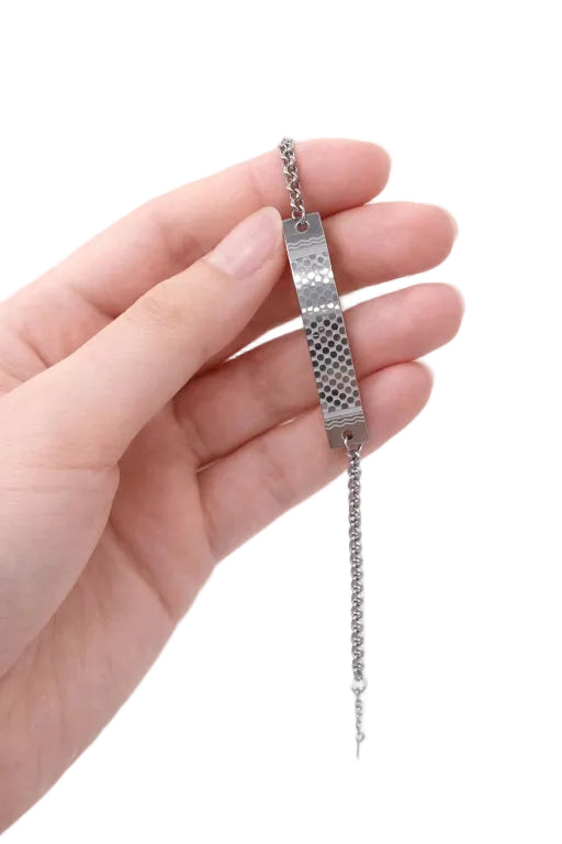 Hand holding a silver bracelet with a textured tag against a white background
